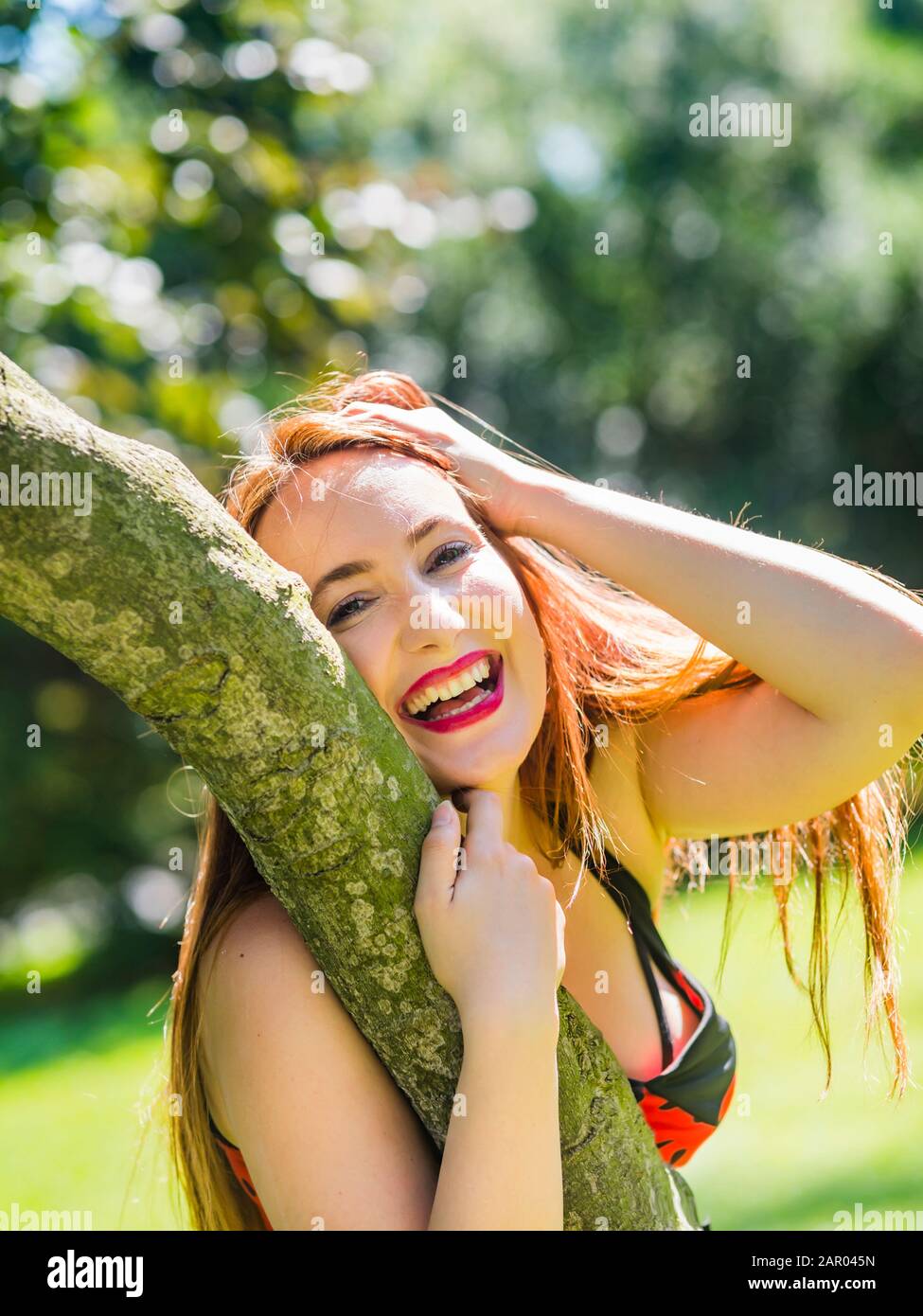 Very happy and laughing portrait inclined on tree in park hand holding head Red-haired redhaired redhair hair Ginger beguiled Stock Photo