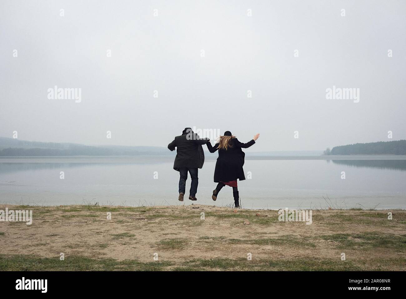 Couple jumping while holding hands on a lake shore Stock Photo