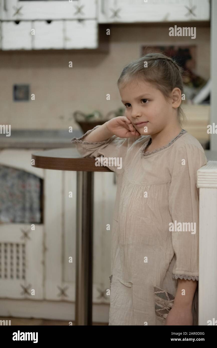 Dark blonde girl in a beige dress in the middle of the kitchen. Stock Photo