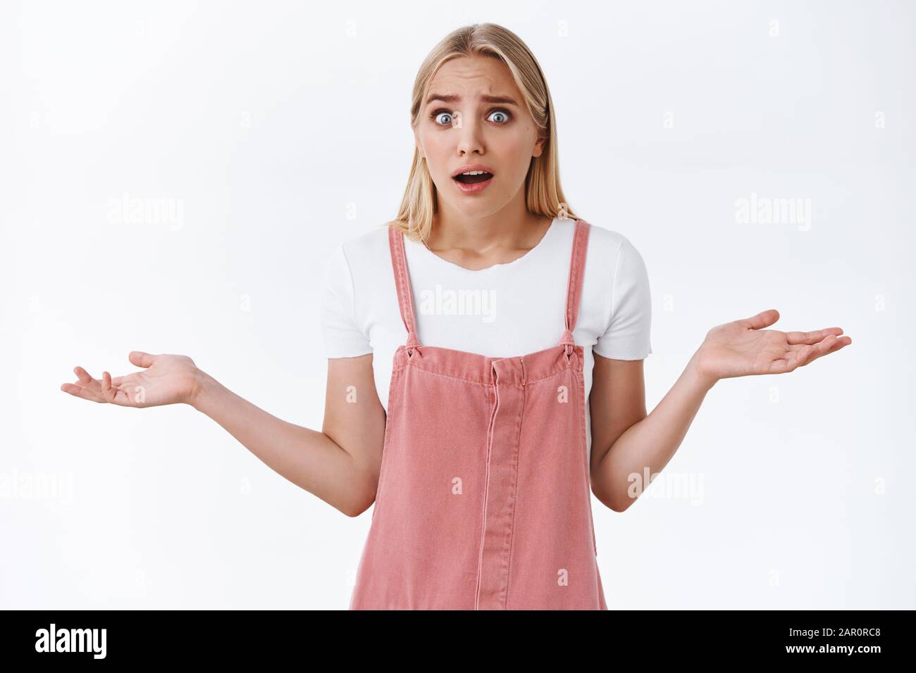 Confused and shocked young blond woman freak-out from strange news, shrugging with hands spread sideways, popping eyes and gasping trying prove her Stock Photo