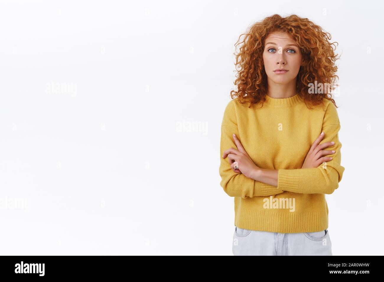 Skeptical attractive redhead curly woman in yellow sweater look with doubt and judgement at camera cross arms chest closed pose listen some strange Stock Photo Alamy
