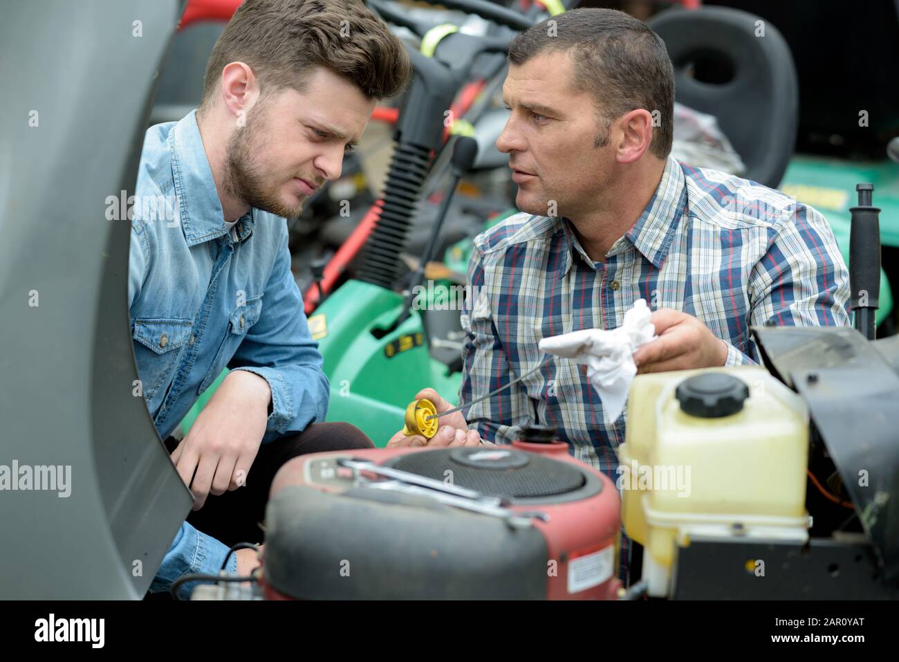 man with apprentice checking oil in lawn mower Stock Photo Alamy
