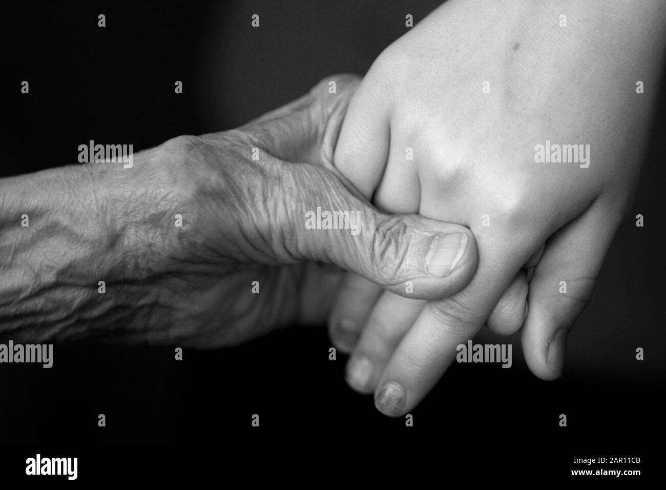 old 90 year old woman holds hand of primary school aged girl in the uk in black and white Stock Photo