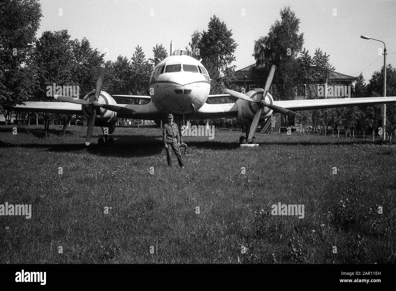 STUPINO, MOSCOW REGION, RUSSIA - CIRCA 1992: A soldier of the Russian army on the background of a Soviet twin-engine military cargo transport aircraft Ilyushin Il-14. Black and white. Film scan. Large grain. Stock Photo