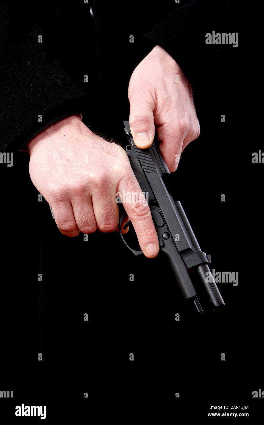 man wearing long dark coat pulling slider back on automatic handgun Stock Photo