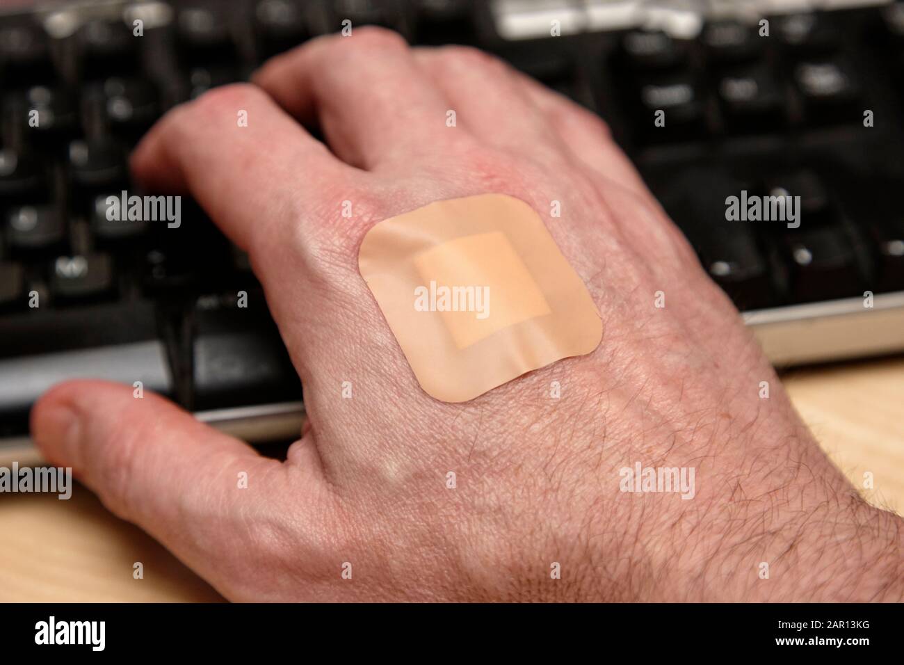 adult mans hand with band-aid adhesive bandage sticking plaster on the back working at keyboard after a blood test for illness Stock Photo
