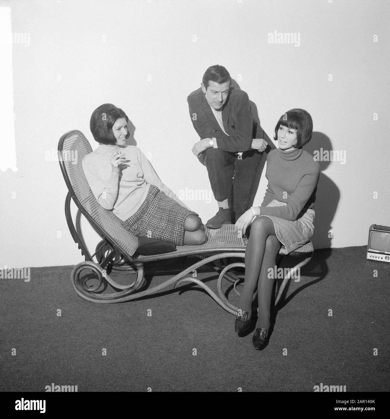 Task Telegraph Annotation: Two young women with turtlenecks and skirts on a wicker lounger in the middle a man in turtleneck. On the right you can see a mini television Date: 28 January 1965 Institution name: Telegraph Stock Photo