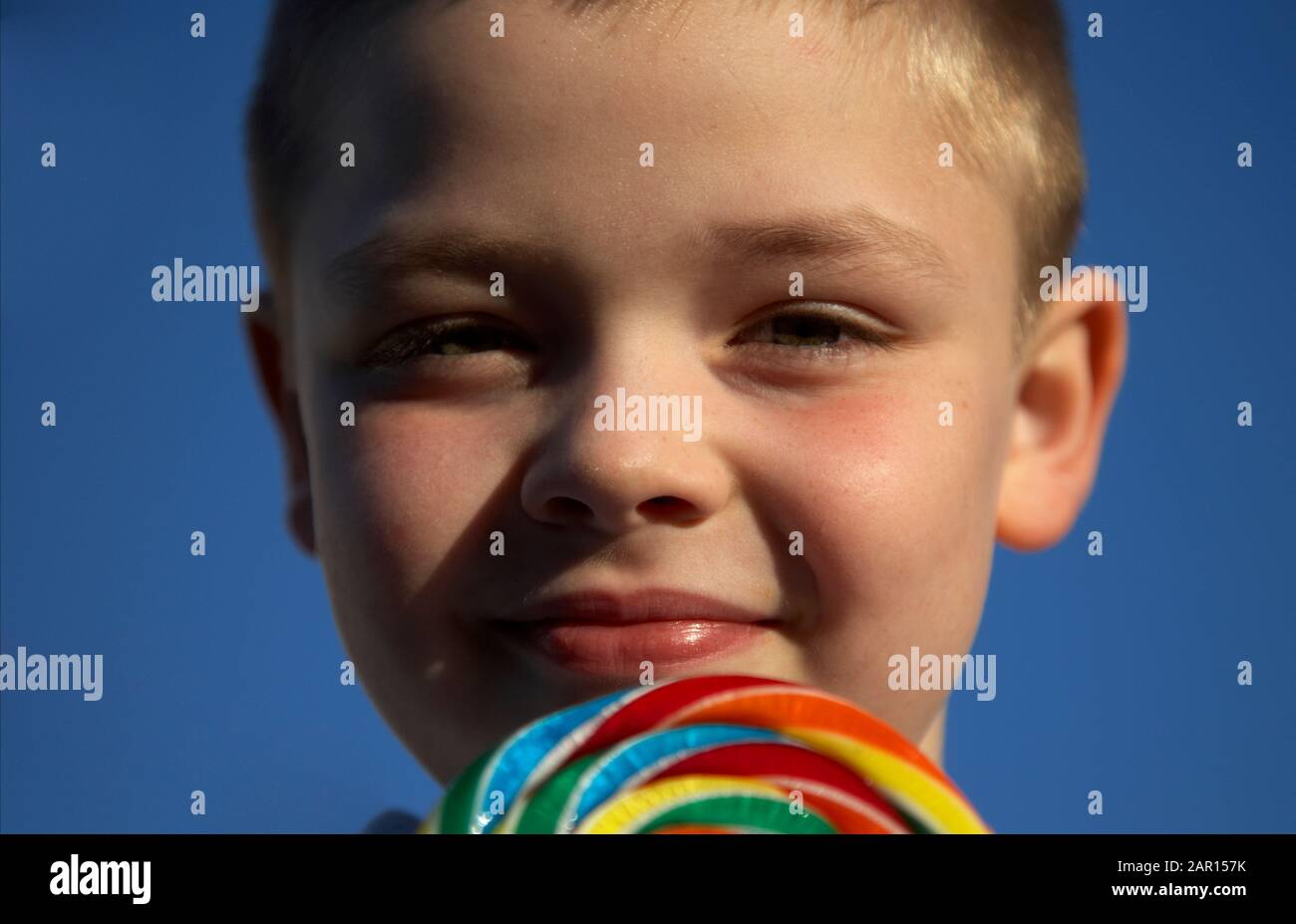 smiling 8 year old boy enjoys eating a sweet lolly Stock Photo