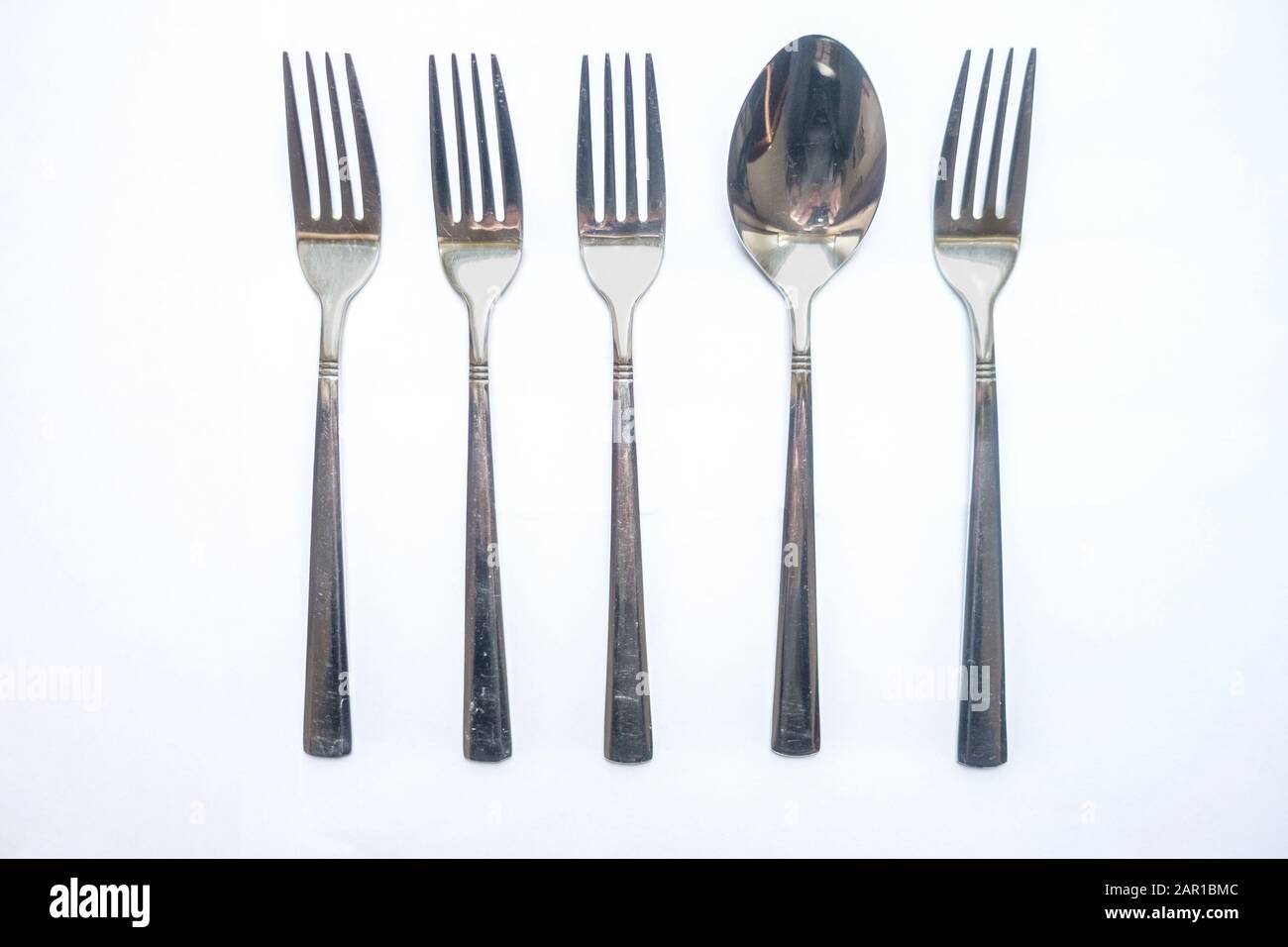 A spoon amongst a row of forks, stands out from the crowd, individuality, different, misfit Stock Photo