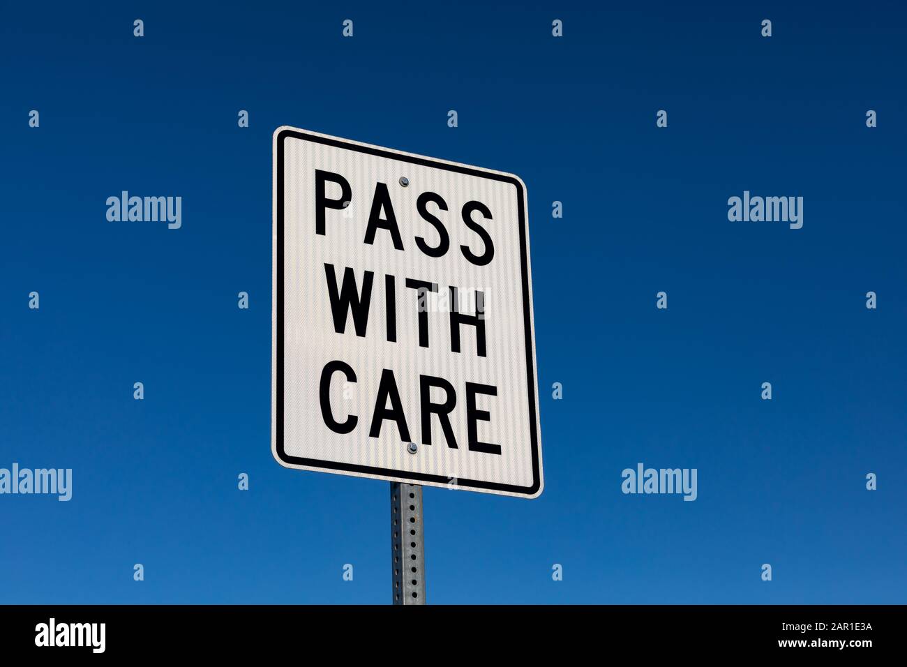 Closeup angled view of pass with care reflective street sign. Isolated on deep blue sky background Stock Photo