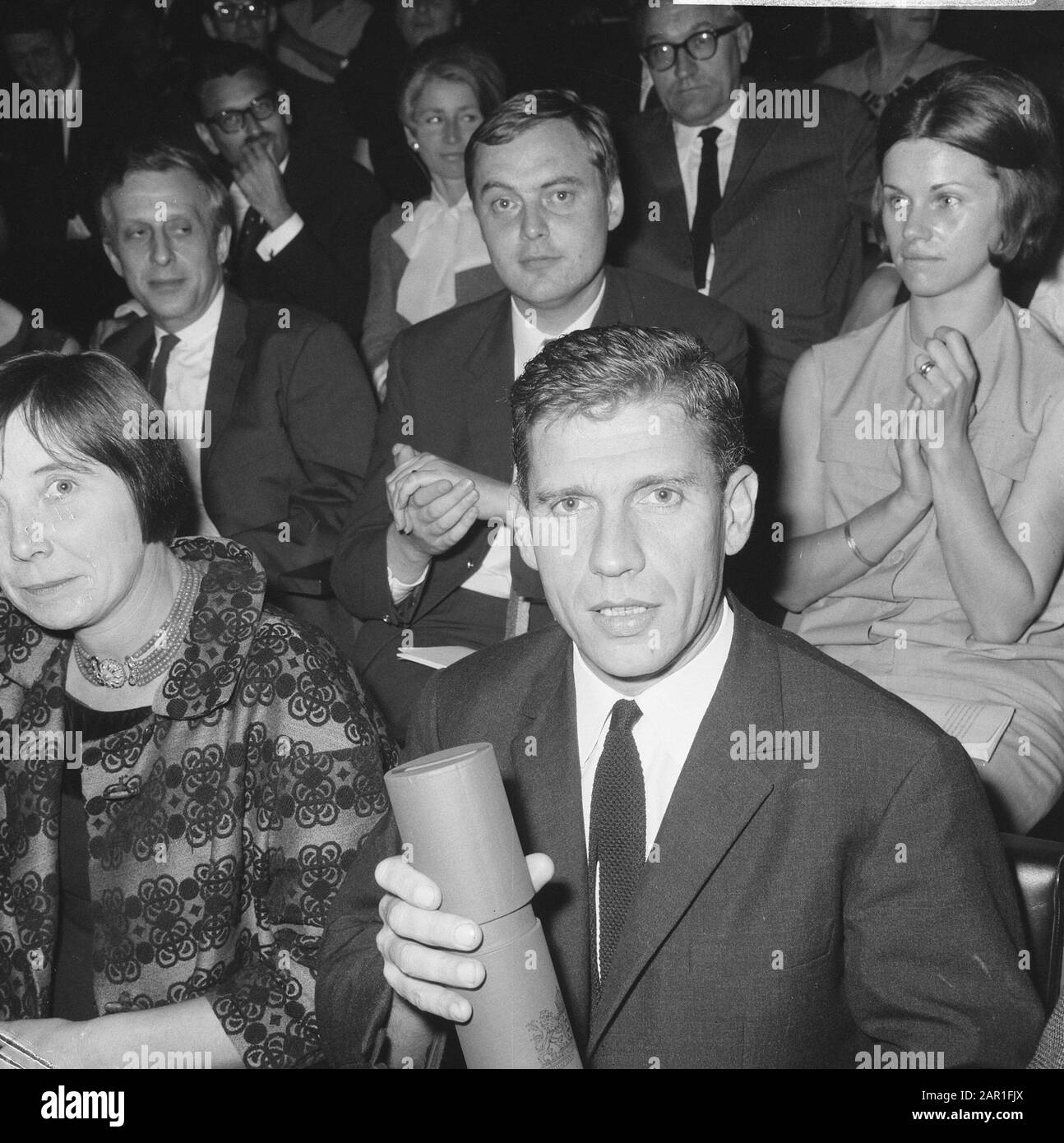 Award to a number of artists of the certificate belonging to the awards awarded by the Municipality of Amsterdam in 1963 and 1964 in the field of art in the David Roëllzaal of the Rijksmuseum in Amsterdam.  In the foreground writer Gerard (Kornelis van de) Reve (for novel prize 1963) and in background graphic designer Baer Cornet (for Frans Duwaerprijs 1963) Date: 15 October 1965 Location: Amsterdam, Noord-Holland Keywords: graphic artists, art, literature, awards, prizes, writers Personal name: Cornet, Baer, Reve, Gerard van de Stock Photo