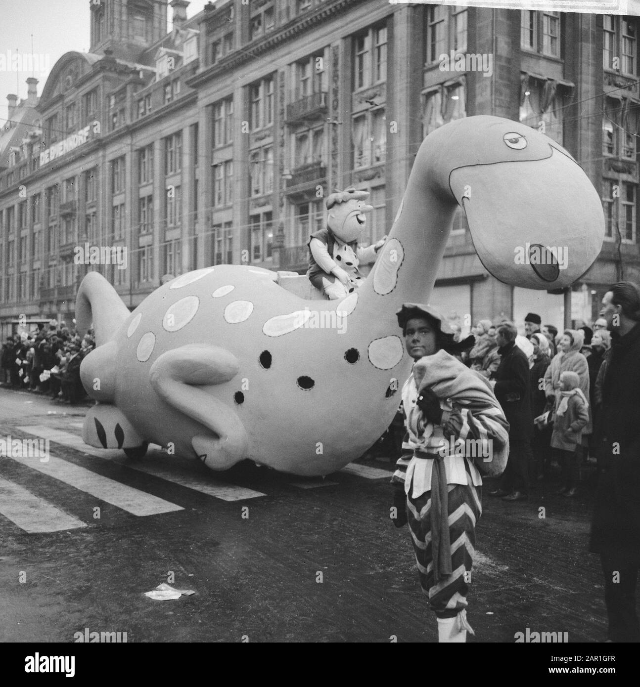 Entry of Saint Nicholas in Amsterdam  Zwarte Piet pose in front of a riding Dino with on his back Barney Rubble from the cartoon series The Flintstones Annotation: In the background department store De Bijenkorf Date: 20 november 1965 Location: Amsterdam, Noord-Holland Keywords: Sinterklaas, Zwarte Piet, public, traditions, folk culture Stock Photo