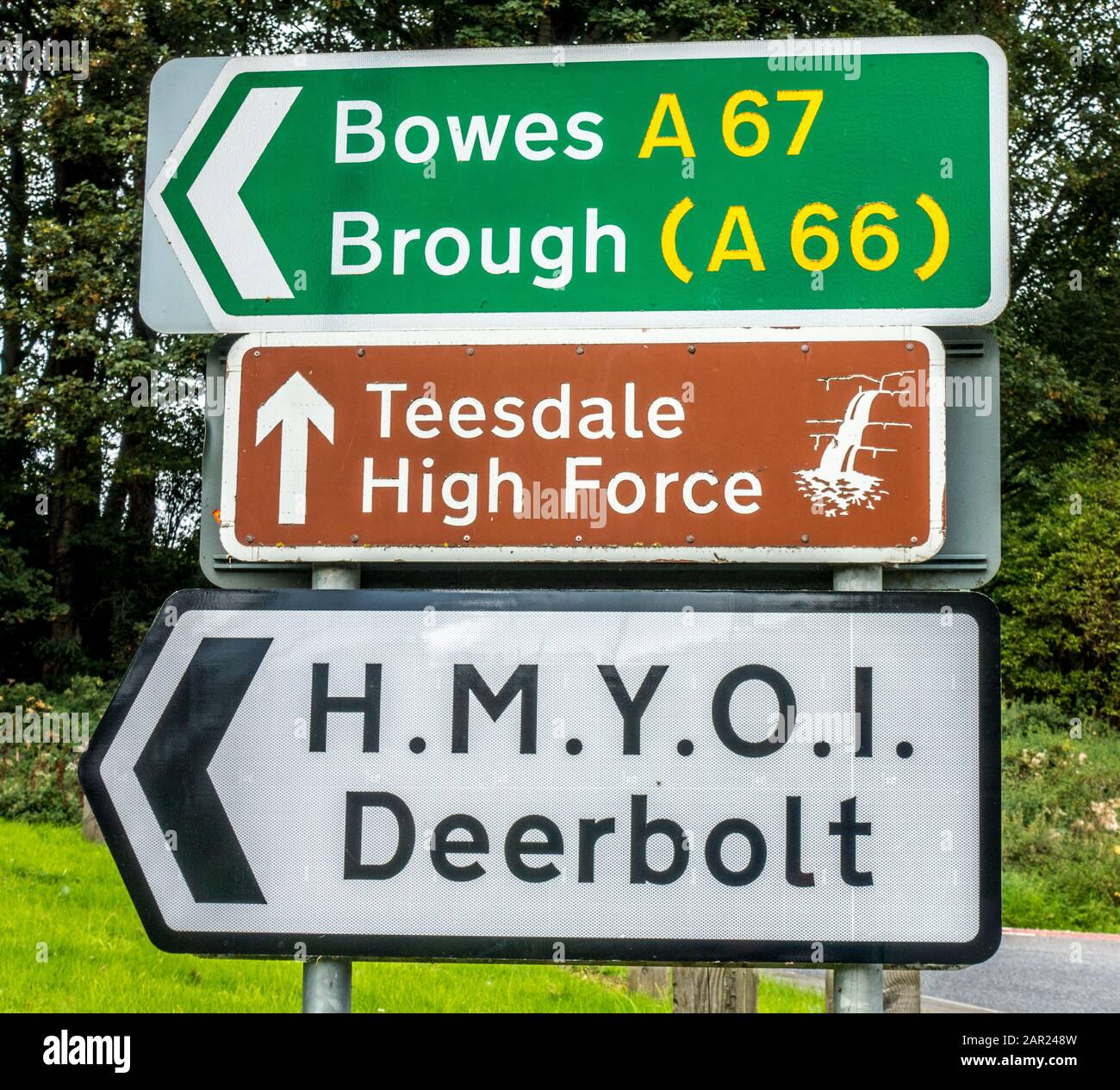 Three direction road signs for Bowes, A67, Brough, A66, Teesdale High Force and H.M.Y.O.I. Deerbolt. Located in Teesdale, County Durham, England, UK. Stock Photo