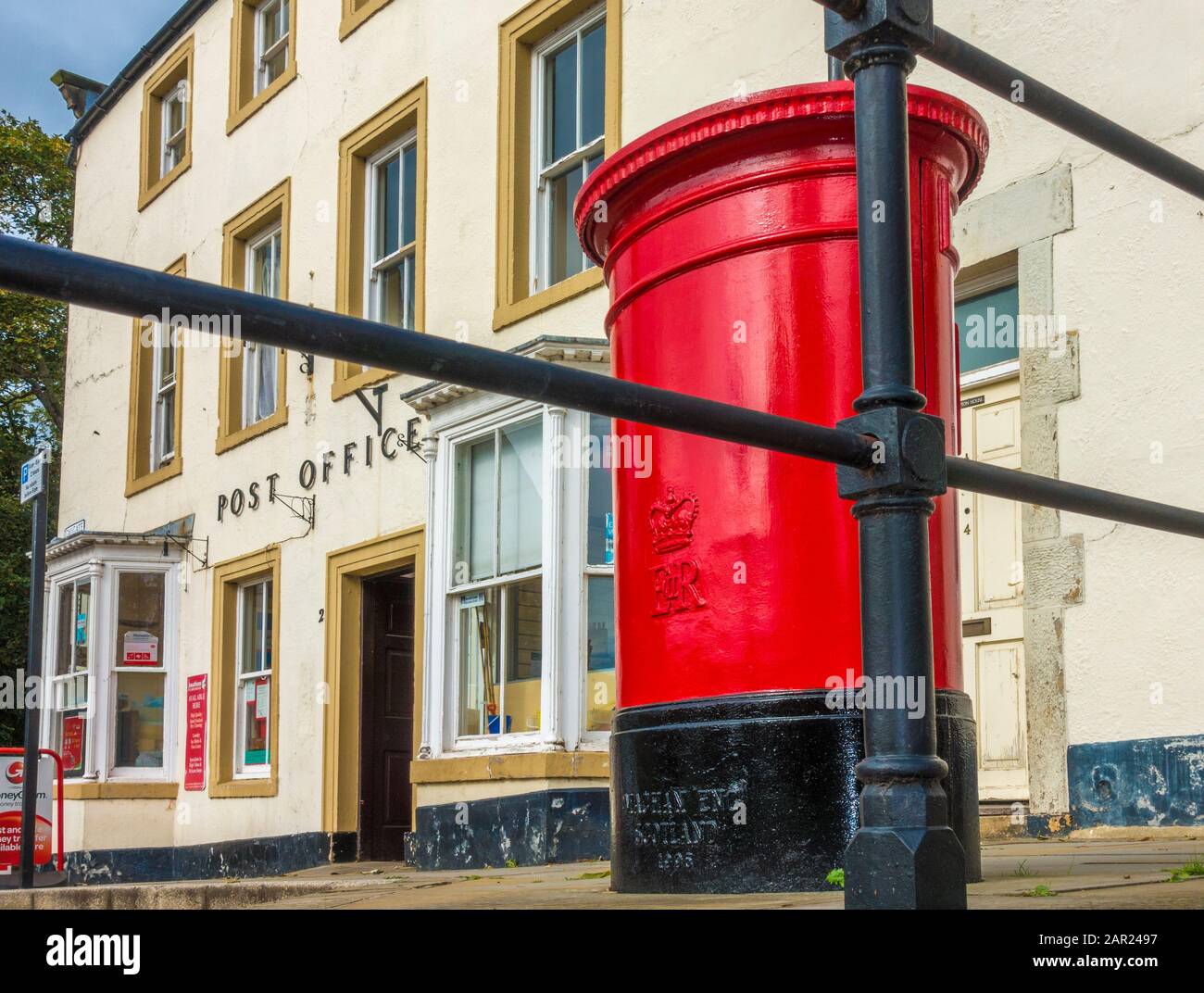 Front of a Post Office in a period building, with a red post box. The
