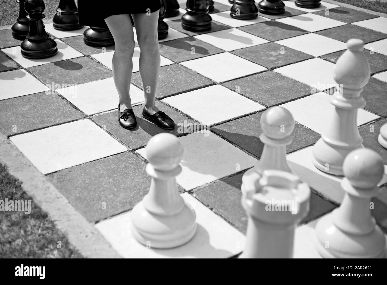 Grey scale shot of a female standing in the middle of a big chess board Stock Photo