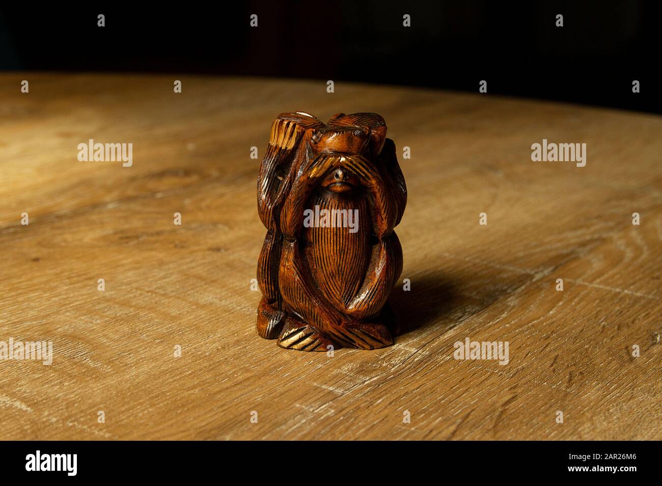 Wooden blindfolded monkey figure on wooden background. I don't see. Three Wise Monkeys - Figurine of chimps depicting 'see no evil' posture. Stock Photo