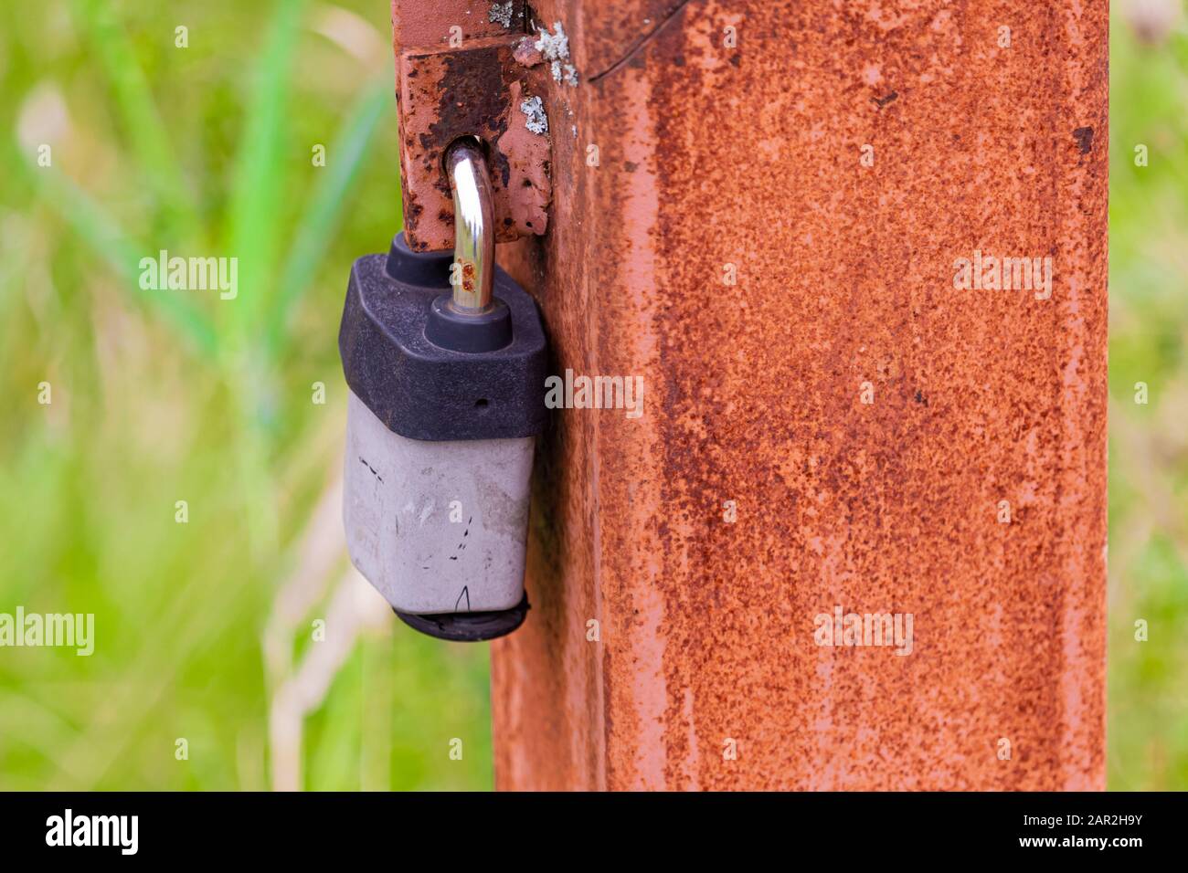 A rusty post along a footpath has a padlock on it, restricting access to an electrical line inside. Stock Photo