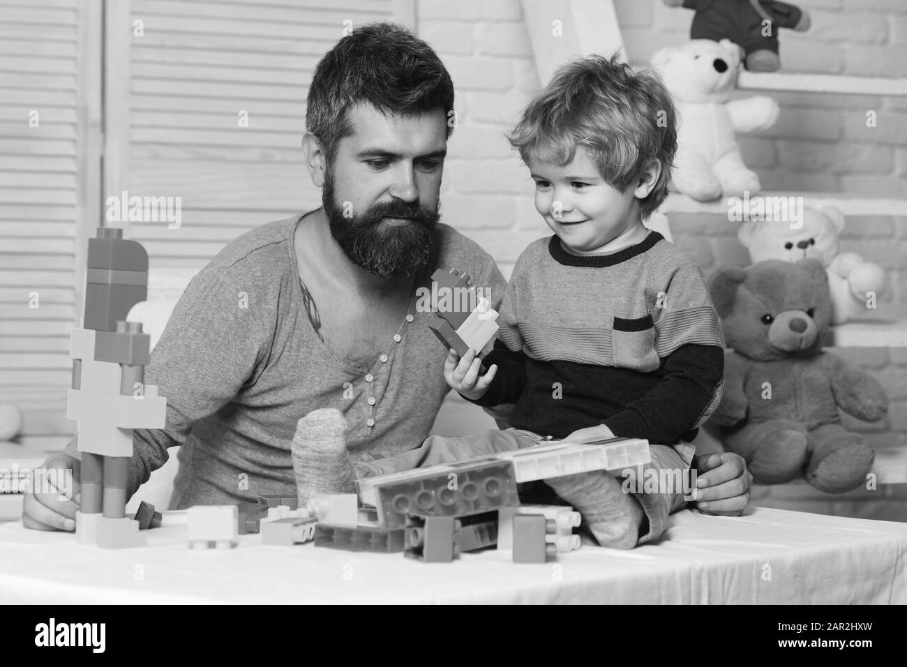 Dad and kid with toys on background build of plastic blocks. Father and son with happy faces create colorful constructions with toy bricks. Family and childhood concept. Man and boy play together Stock Photo