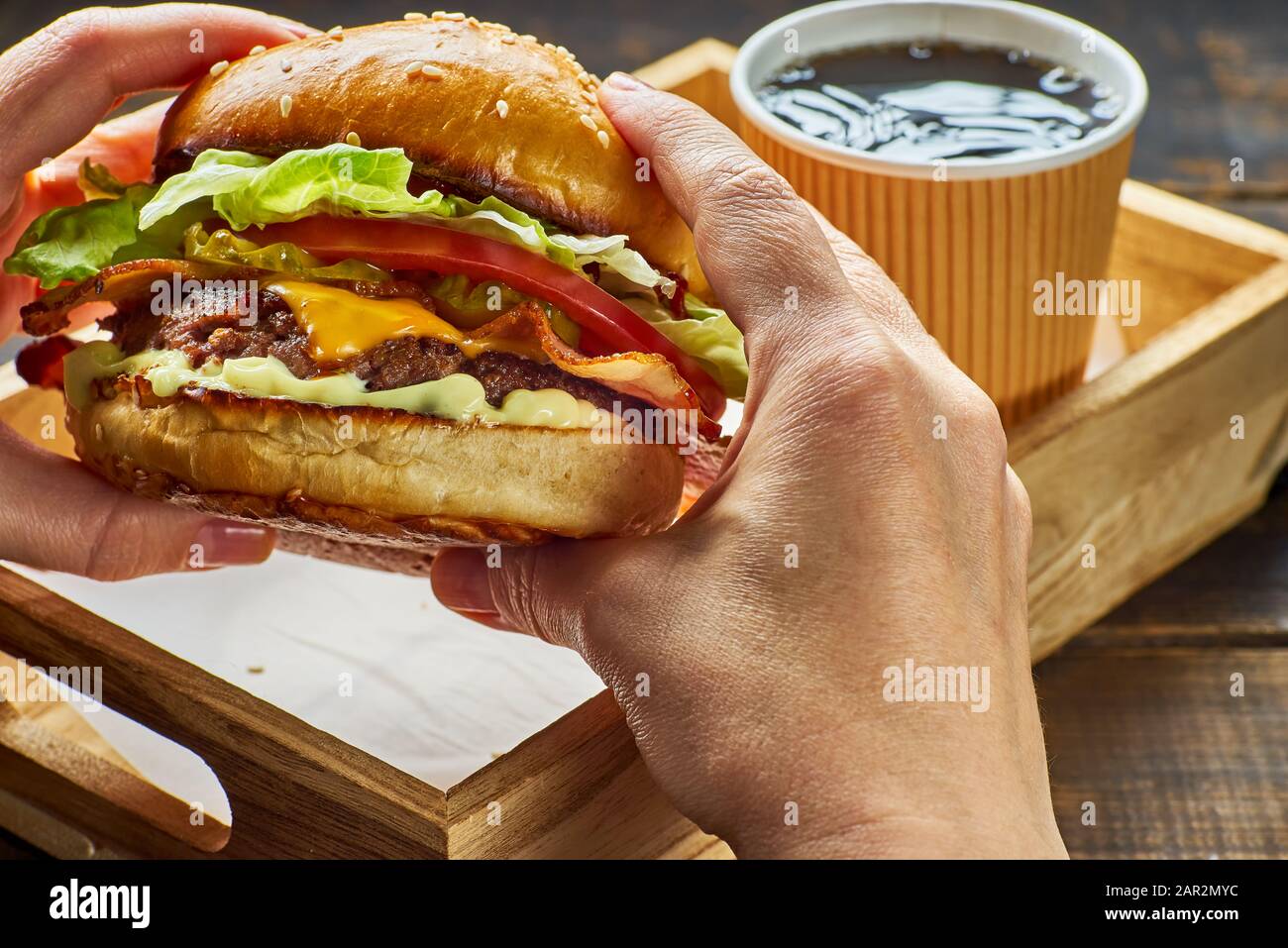 Woman's hands holding a hamburger over wooden tray and paper cup of drink Stock Photo