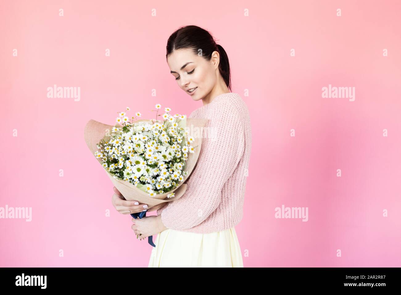 Girl in a dress with a bouqet of flowers chamomile on a pink background ...