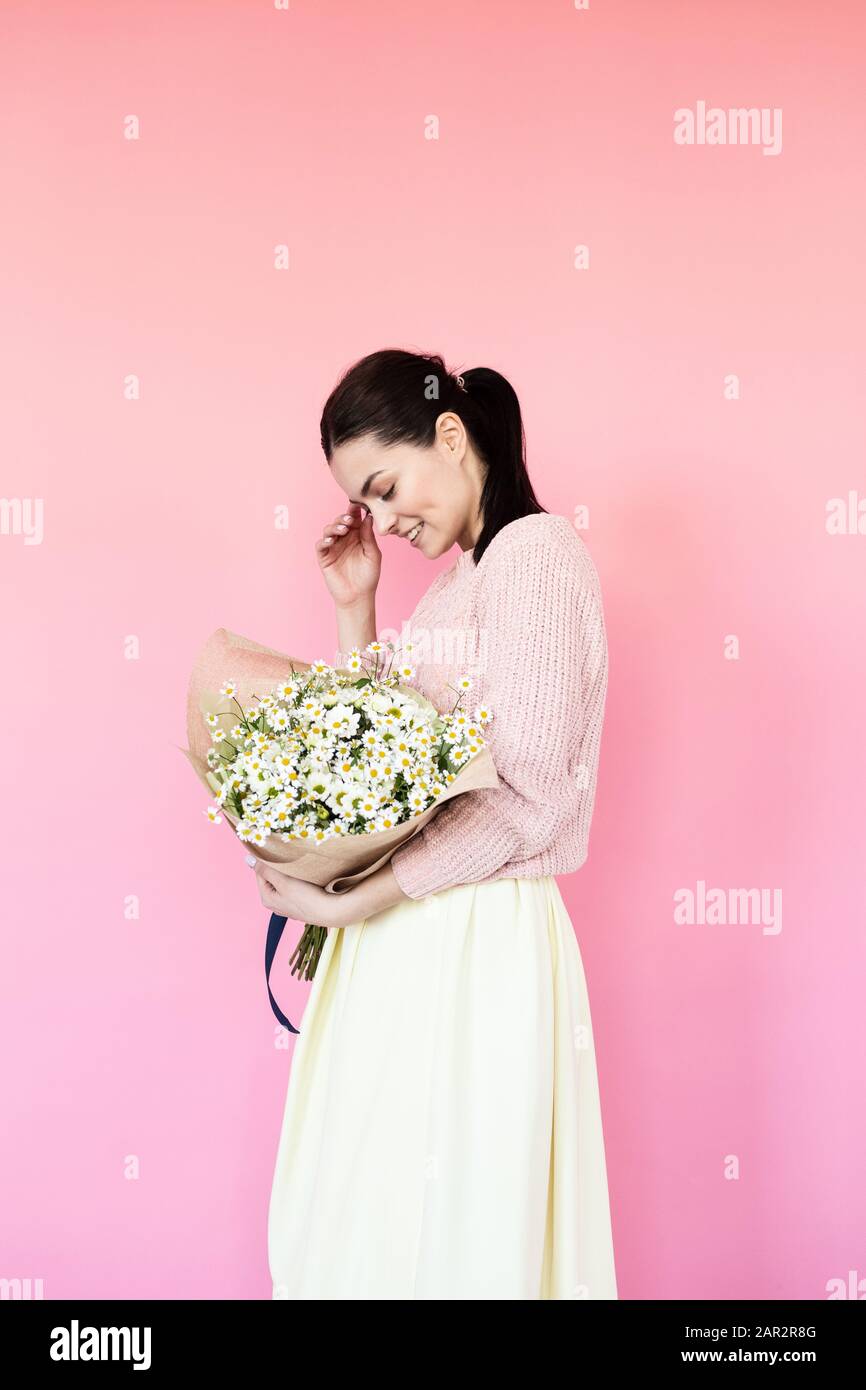 Girl in a dress with a bouqet of flowers chamomile on a pink background ...