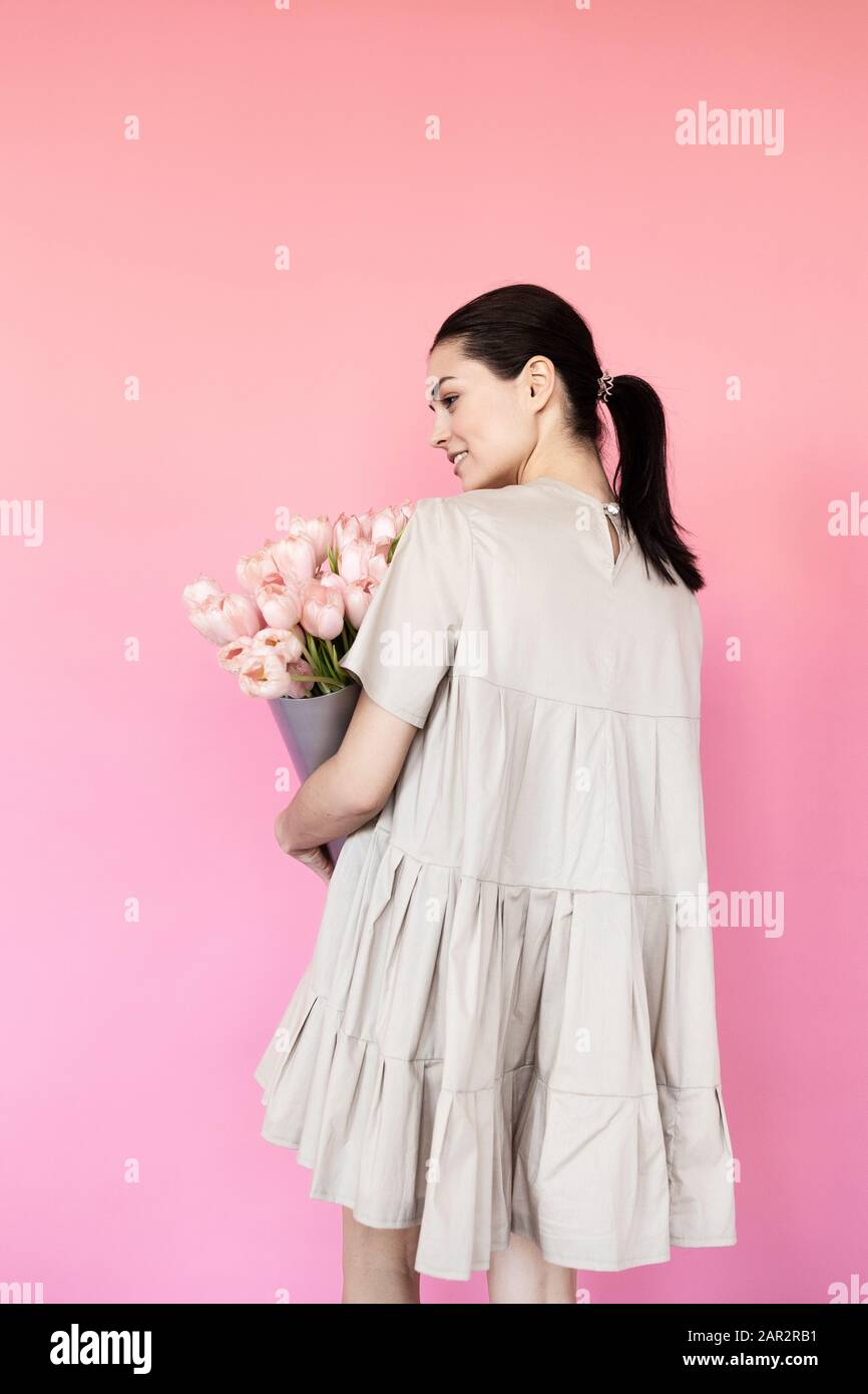 Girl in a dress with a bouqet of flowers chamomile on a pink background ...