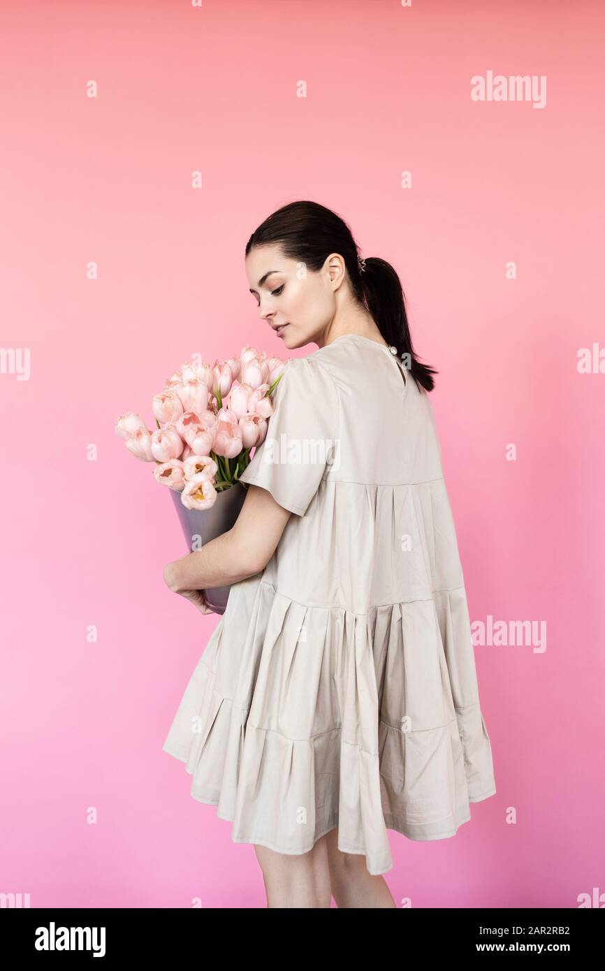 Girl in a dress with a bouqet of flowers chamomile on a pink background ...