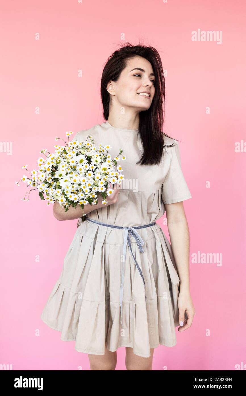 Girl in a dress with a bouqet of flowers chamomile on a pink background ...