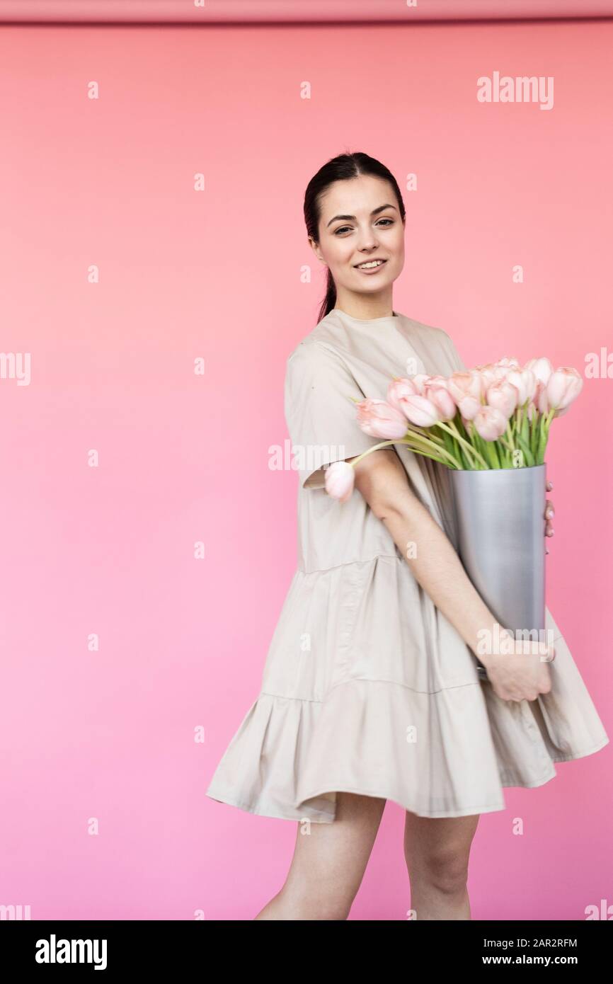 Girl in a dress with a bouqet of flowers chamomile on a pink background ...