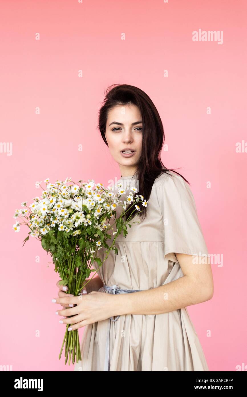 Girl in a dress with a bouqet of flowers chamomile on a pink background ...