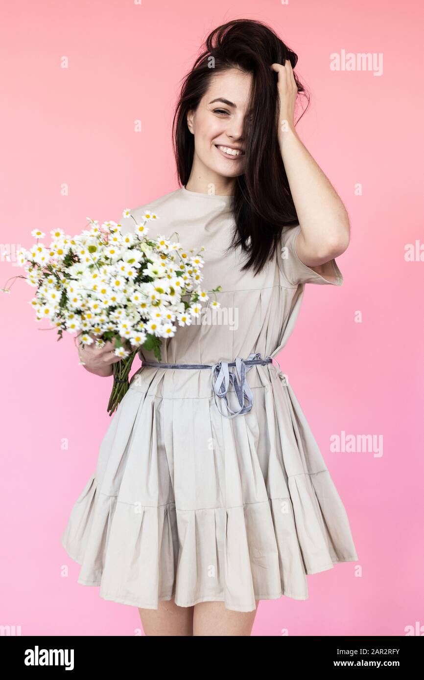 Girl in a dress with a bouqet of flowers chamomile on a pink background ...