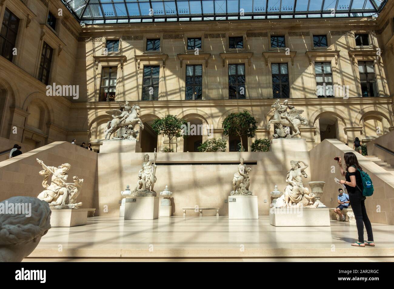 A visitor taking photos in the Cour Marly sculpture courtyard in