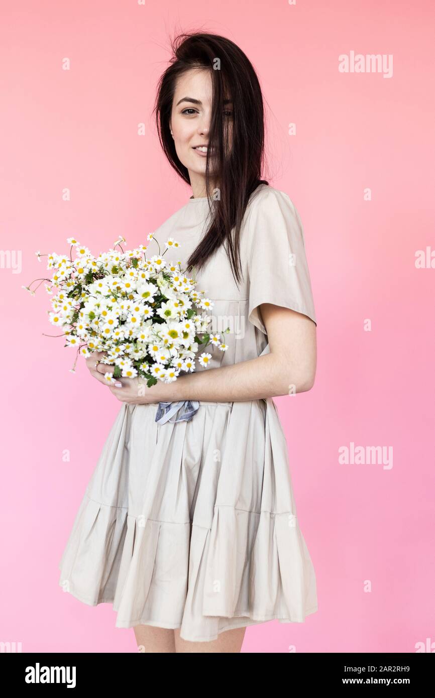 Girl in a dress with a bouqet of flowers chamomile on a pink background ...