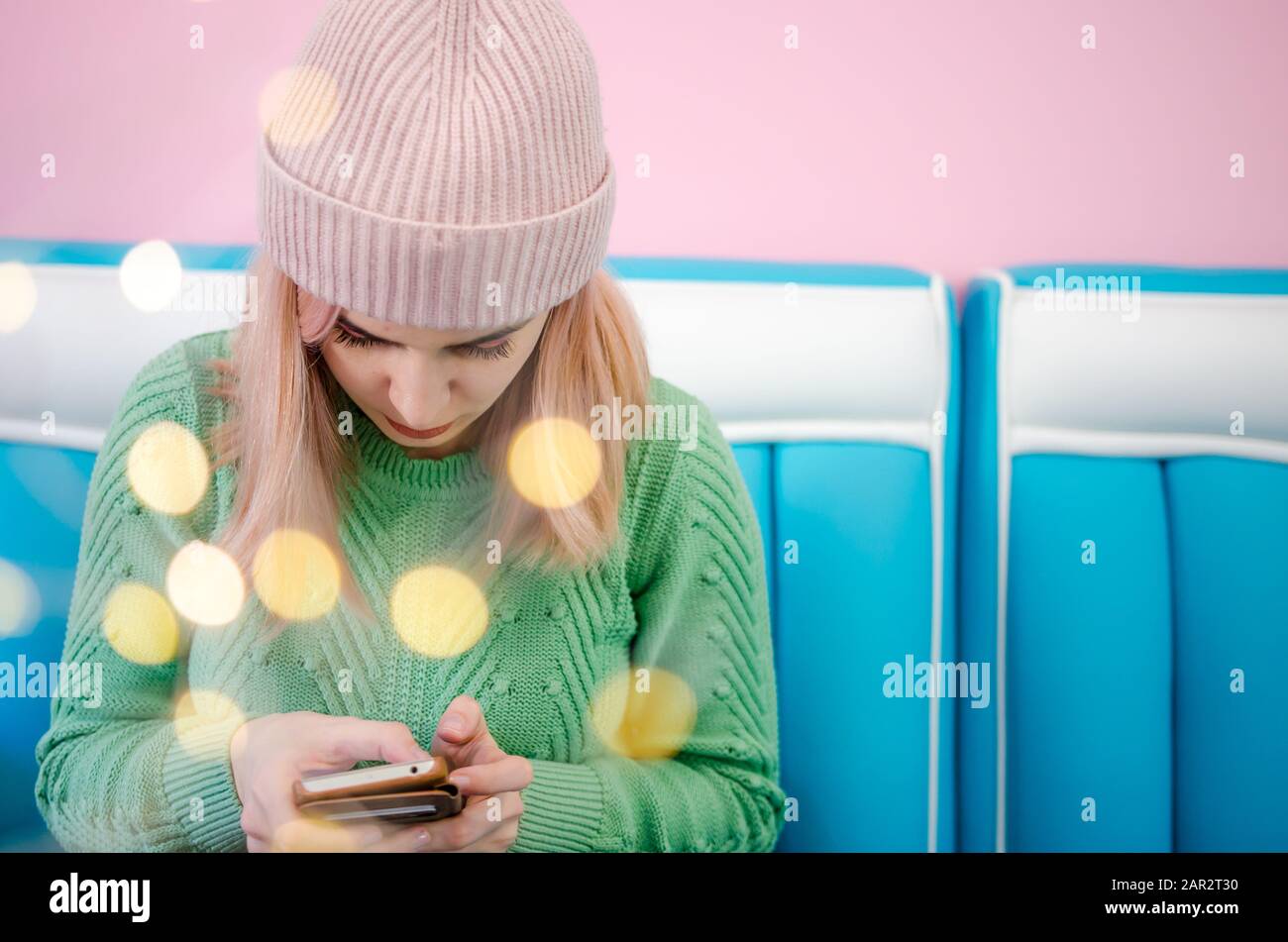 Pretty young woman holding mobile phone in hands. Portrait of a lovely girl in green sweater with bokeh lights Stock Photo