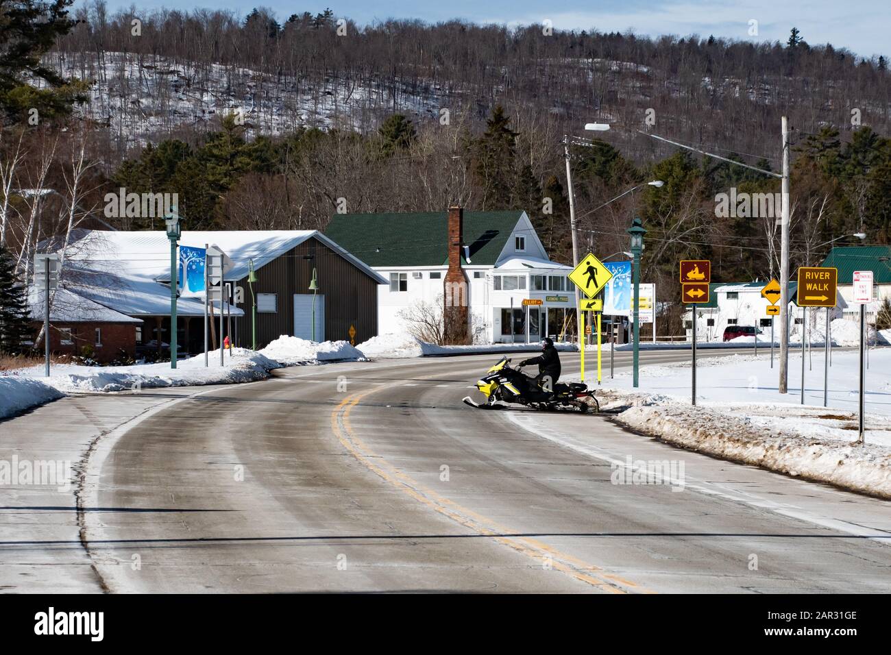 A snowmobile crossing the highway between a parking lot and Lake
