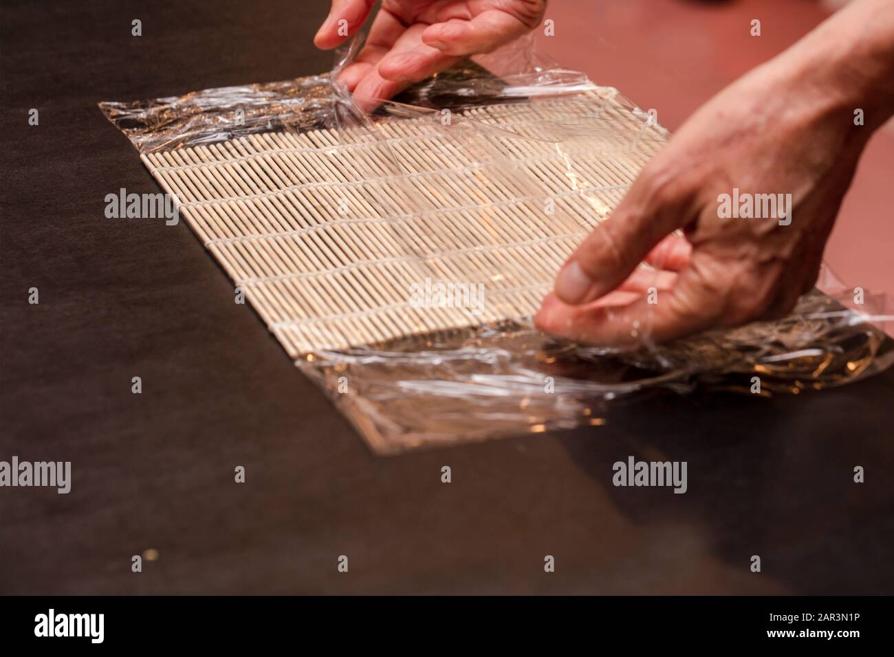 Chef Preparing Sushi Mat With Plastic Wrap To Make A Roll For A