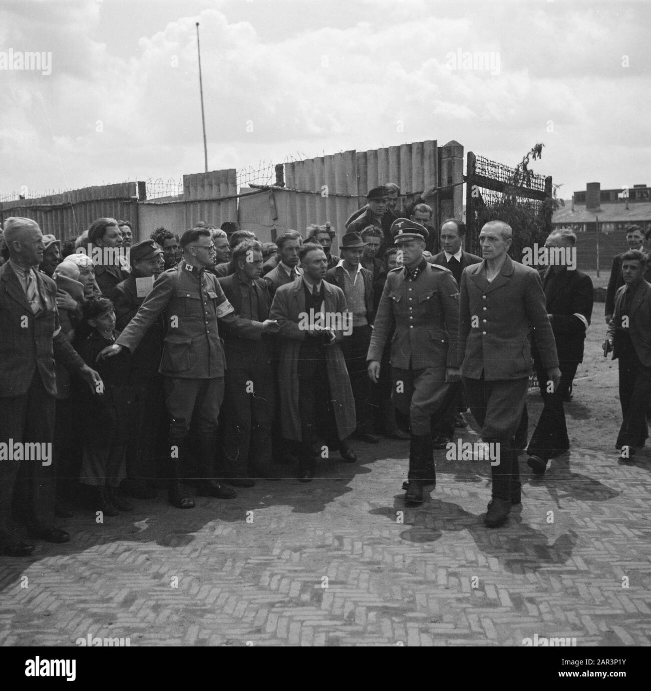 Camp Amersfoort, internment camp for war criminals and collaborators  SS camp guard B.J. Westerveld (right) and camp commander K.P. Berg walk past a crowd Annotation: Left a woman with a baby. her head a kind of cloth with aviator glasses Date: 1945 Location: Amersfoort Keywords: prisoners, internment camps, war crimes, Second World War Personname: Berg, K.P., Westerveld, B.J. Stock Photo