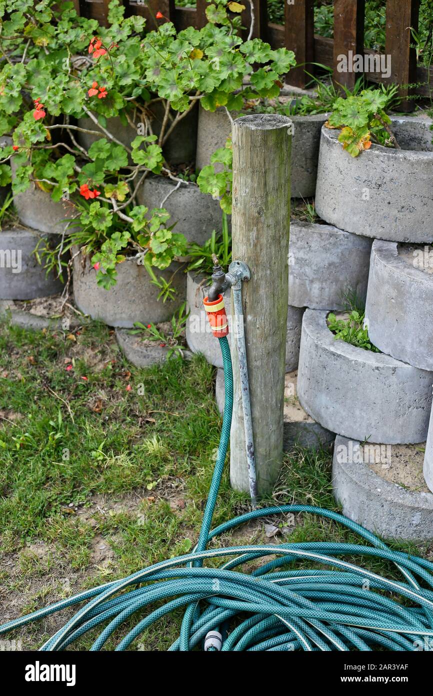 A Vertical Shot Of A Water Hose Near The Cement Flower Pots In A