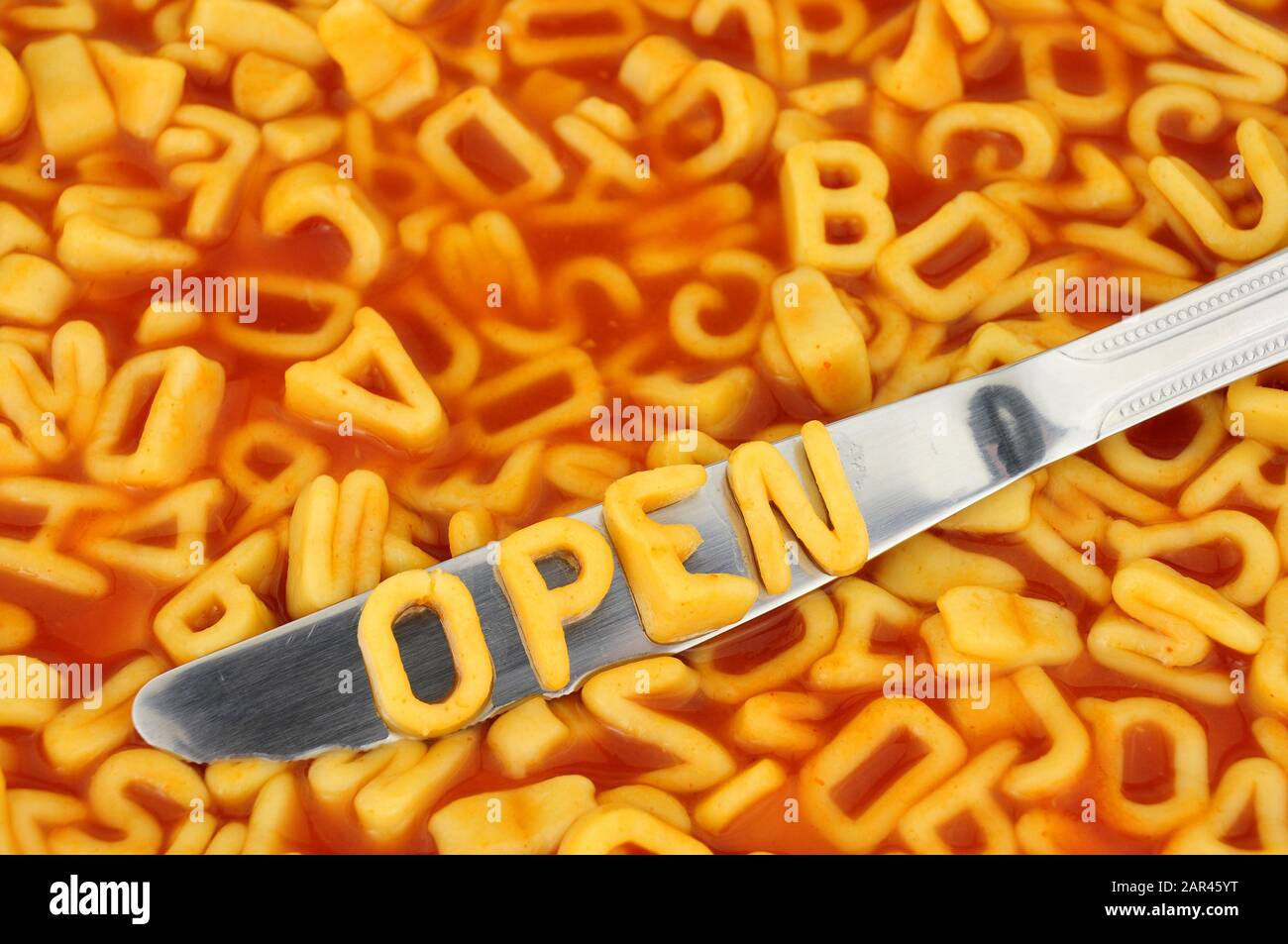 Alphabet spaghetti spelling open with random letters in tomato sauce background Stock Photo