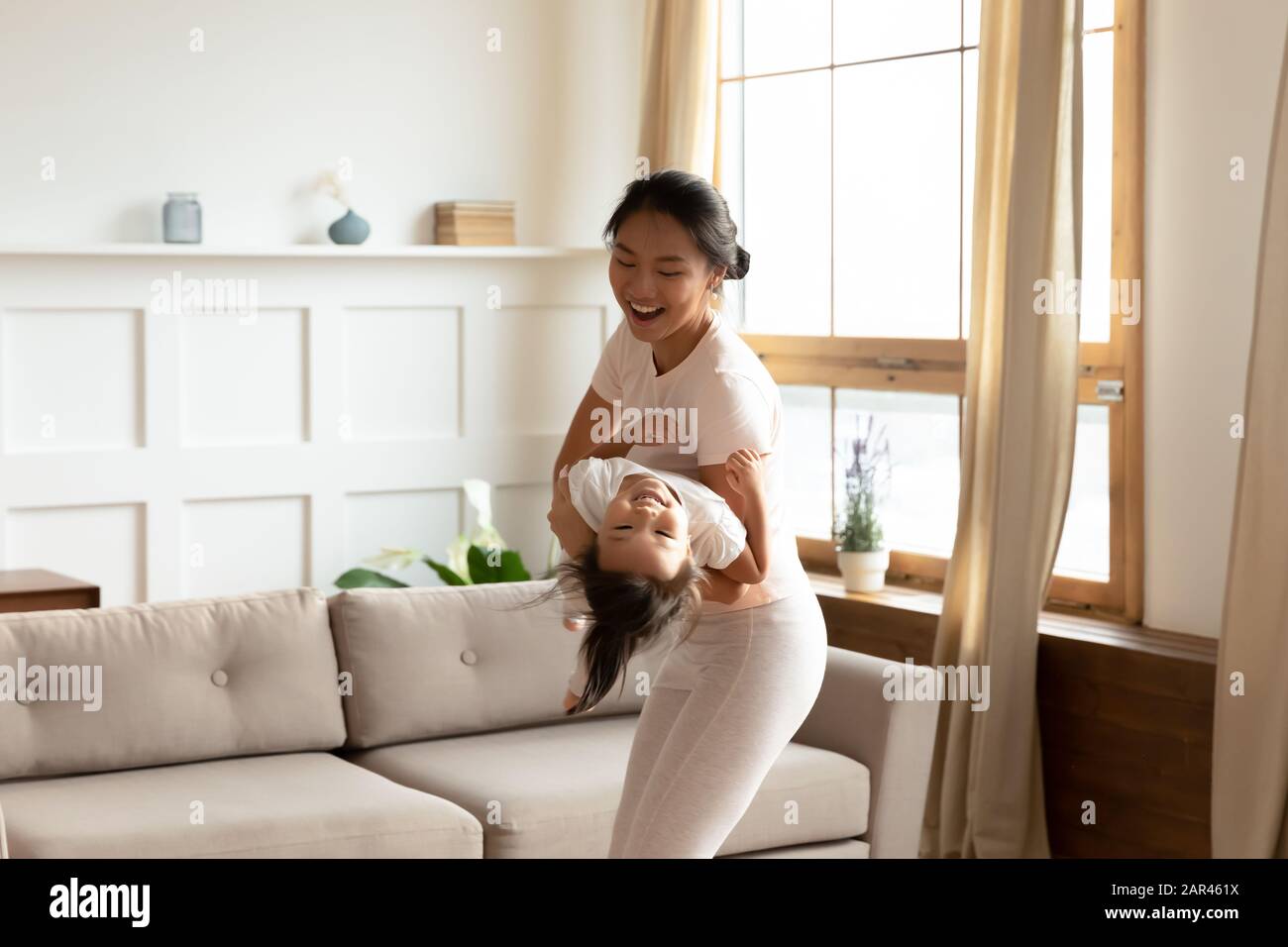 Overjoyed Vietnamese mom and small daughter have fun at home Stock Photo