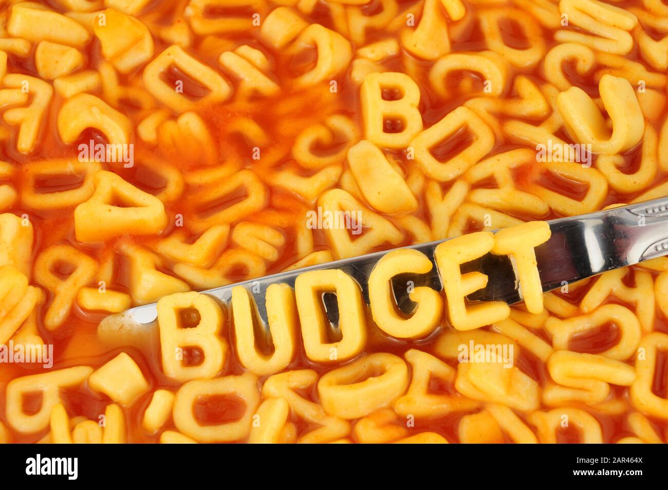 Alphabet spaghetti spelling budget with random letters in tomato sauce background Stock Photo