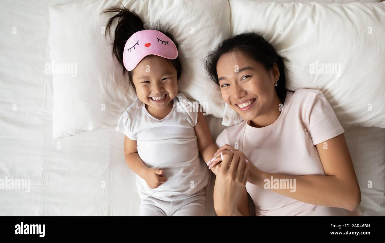 Overjoyed Asian young mum and small daughter lying in bed Stock Photo