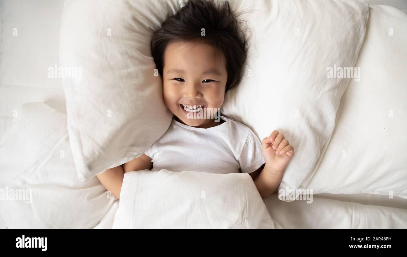 Overjoyed Asian small girl awaken in home bed Stock Photo