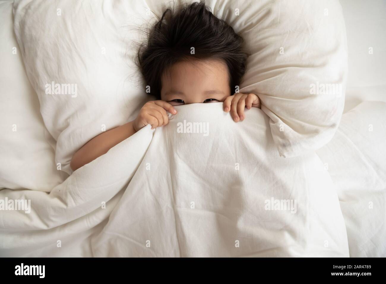Happy little Asian girl hide under blanket in bed Stock Photo