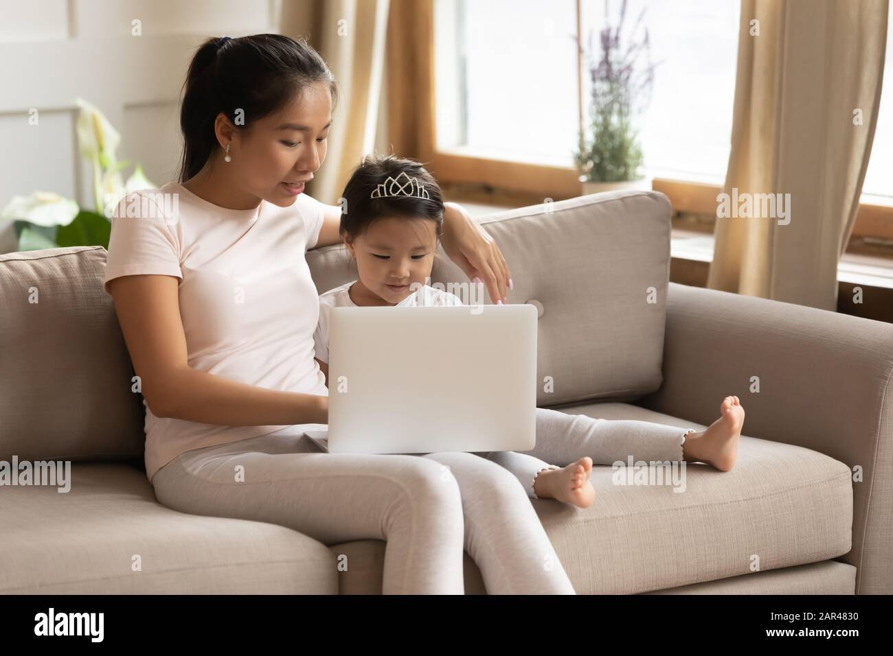 Young Asian mom and daughter using laptop together Stock Photo