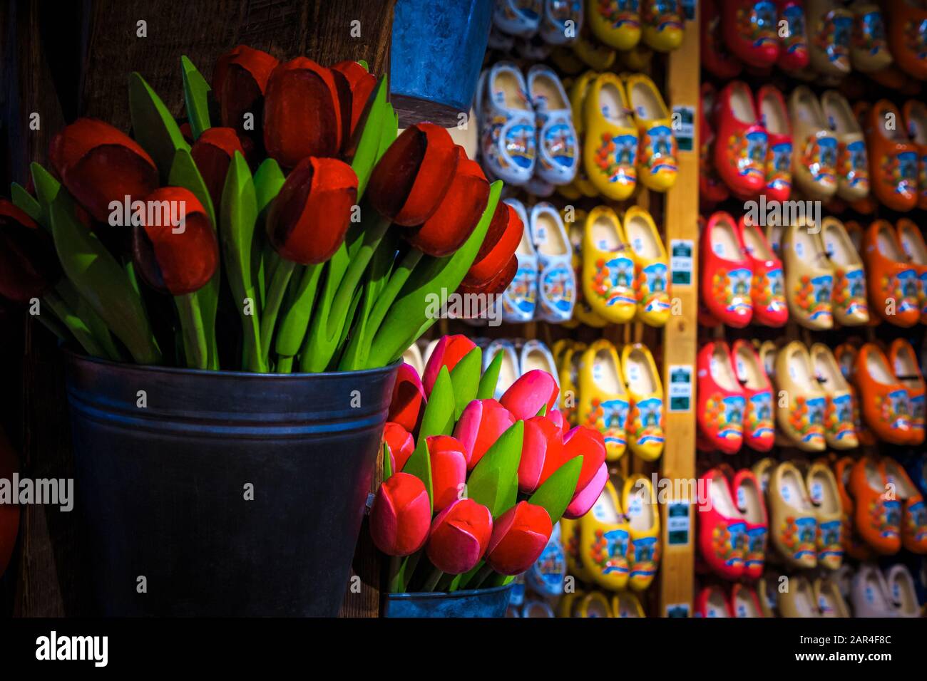 Stunning colorful bouquets of wooden tulips in the bucket and wooden shoes in row on the wall. Dutch souvenir shop decoration with handmade gift objec Stock Photo