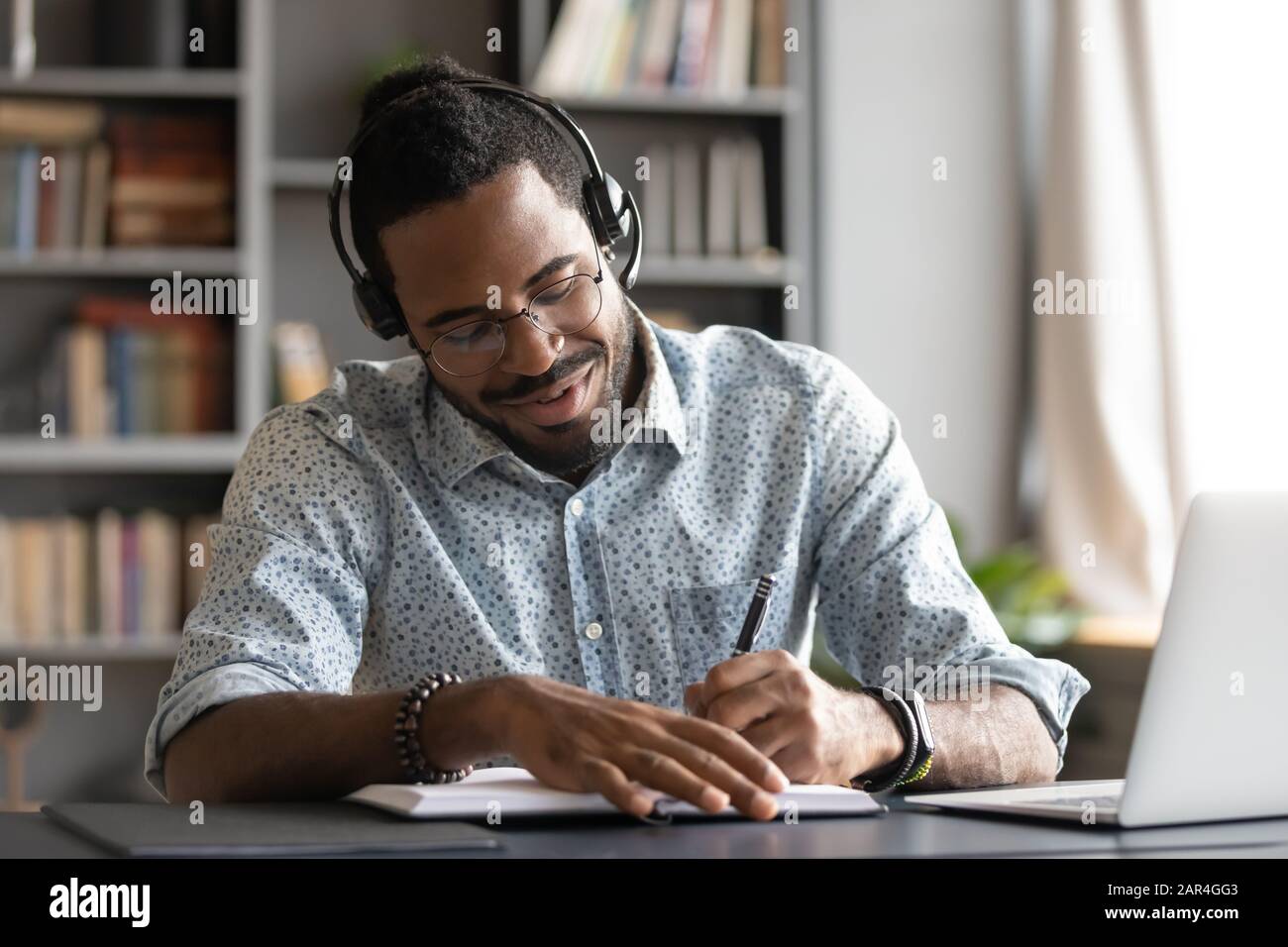 Smiling african male student professional wear headset elearning making notes Stock Photo