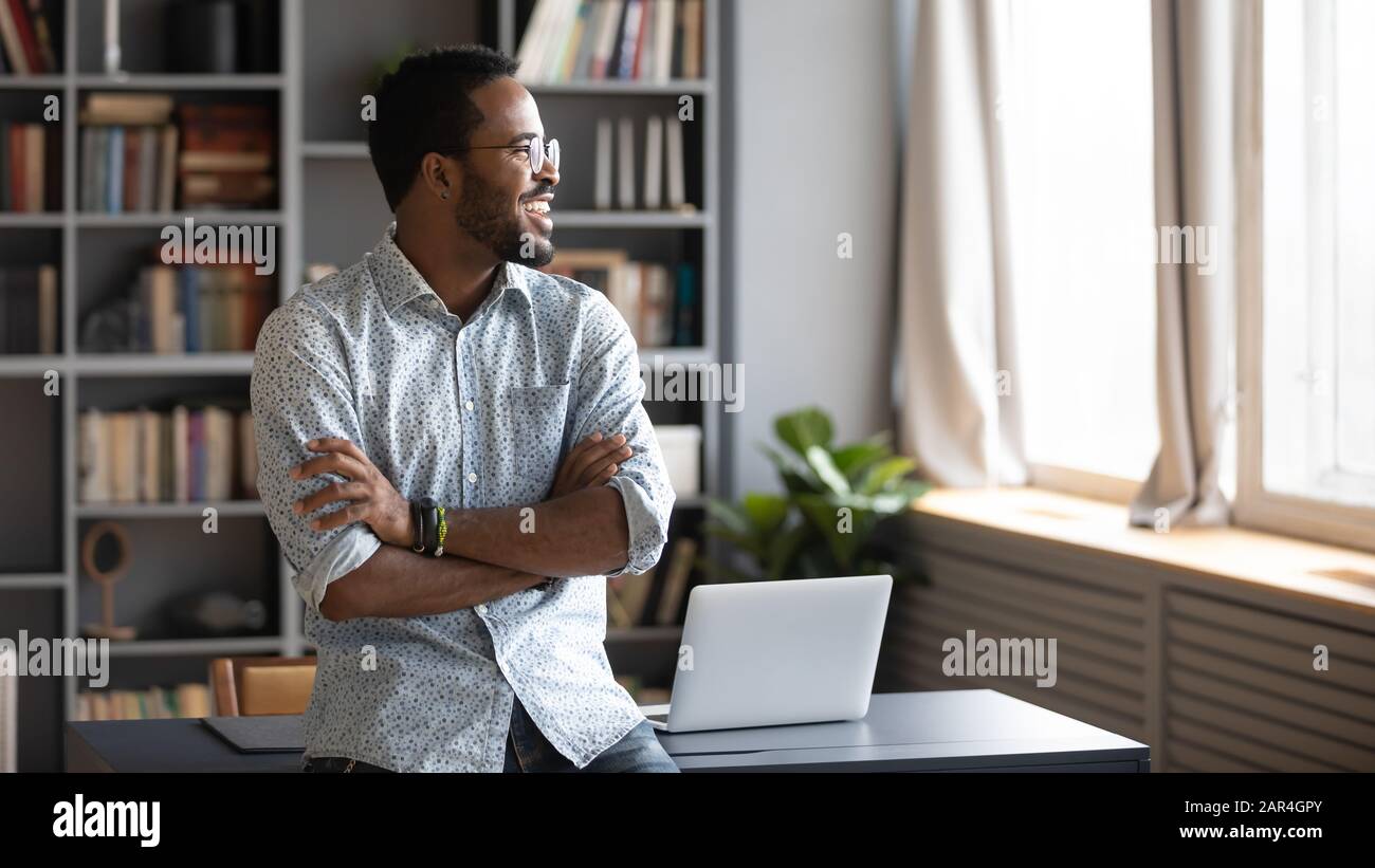 Happy african business man looking away dreaming standing in office Stock Photo