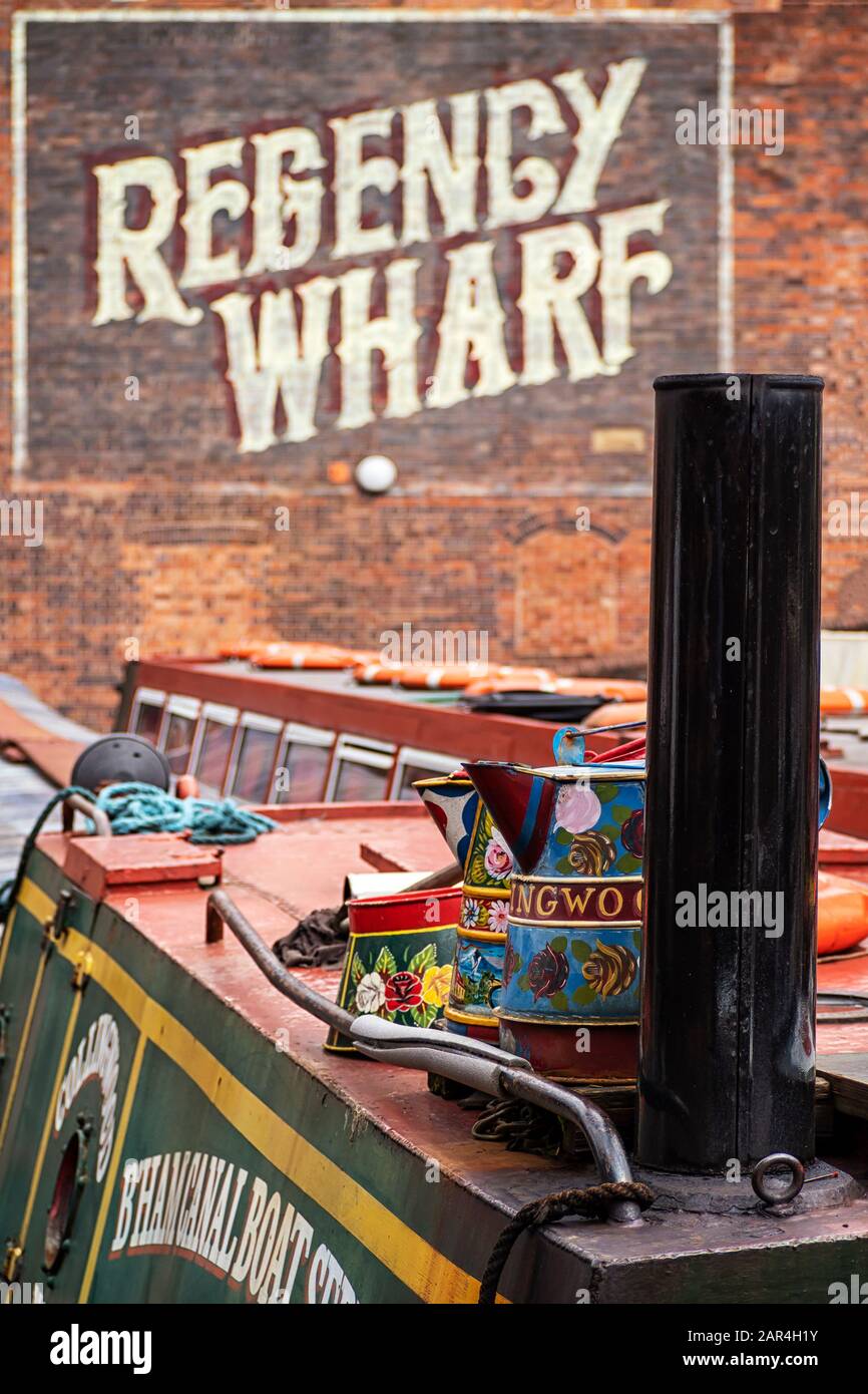 BIRMINGHAM, UK - MAY 28, 2019:  Brightly painted narrowboat on the canal at Brindley Place moored in front of the Victorian Regency Wharf with sign Stock Photo