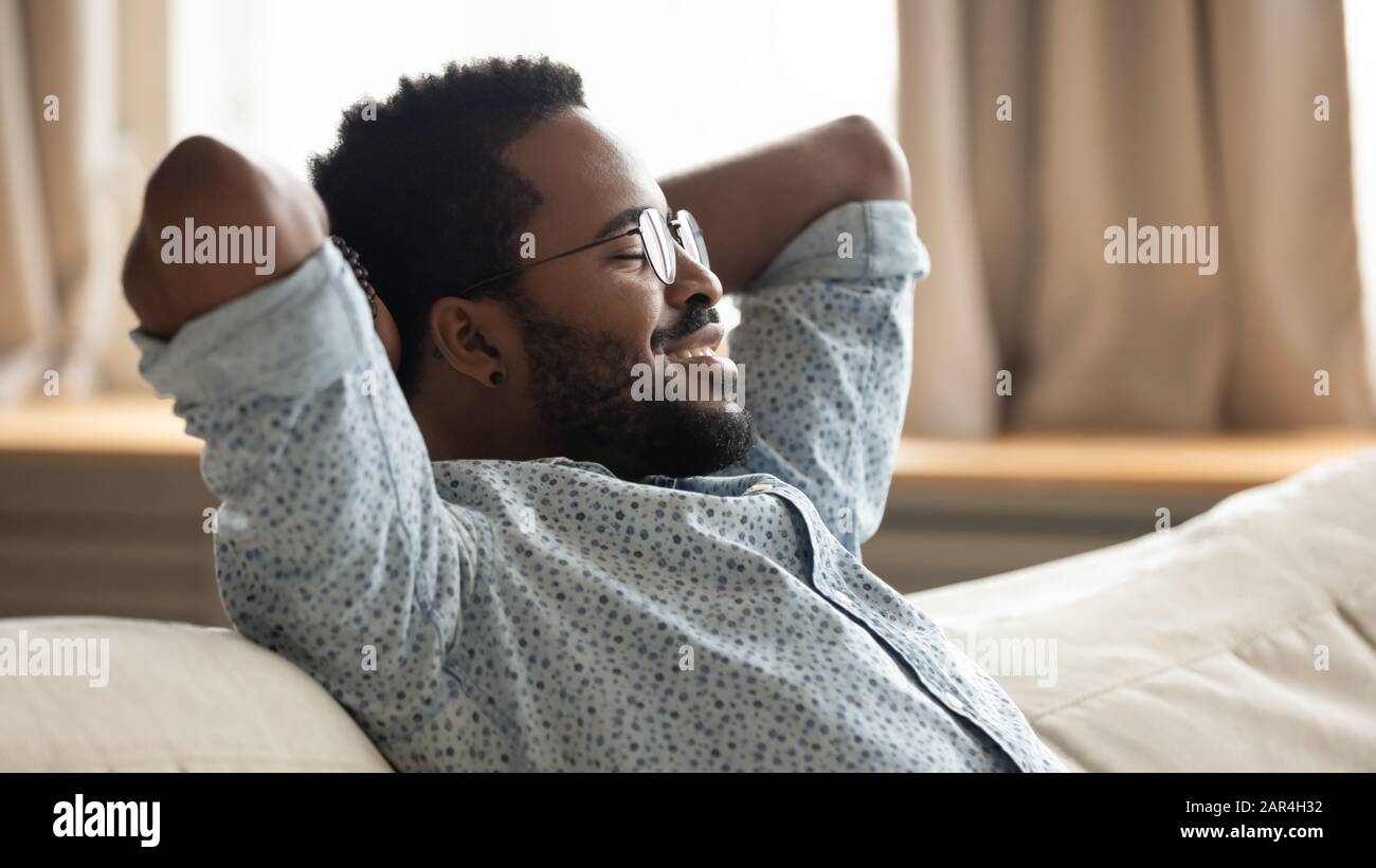 Happy african guy relaxing on couch eyes closed breathing air Stock Photo
